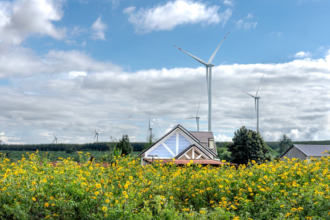 Charming rural landscape with wind turbines behind sunflowers and houses under a bright summer sky.