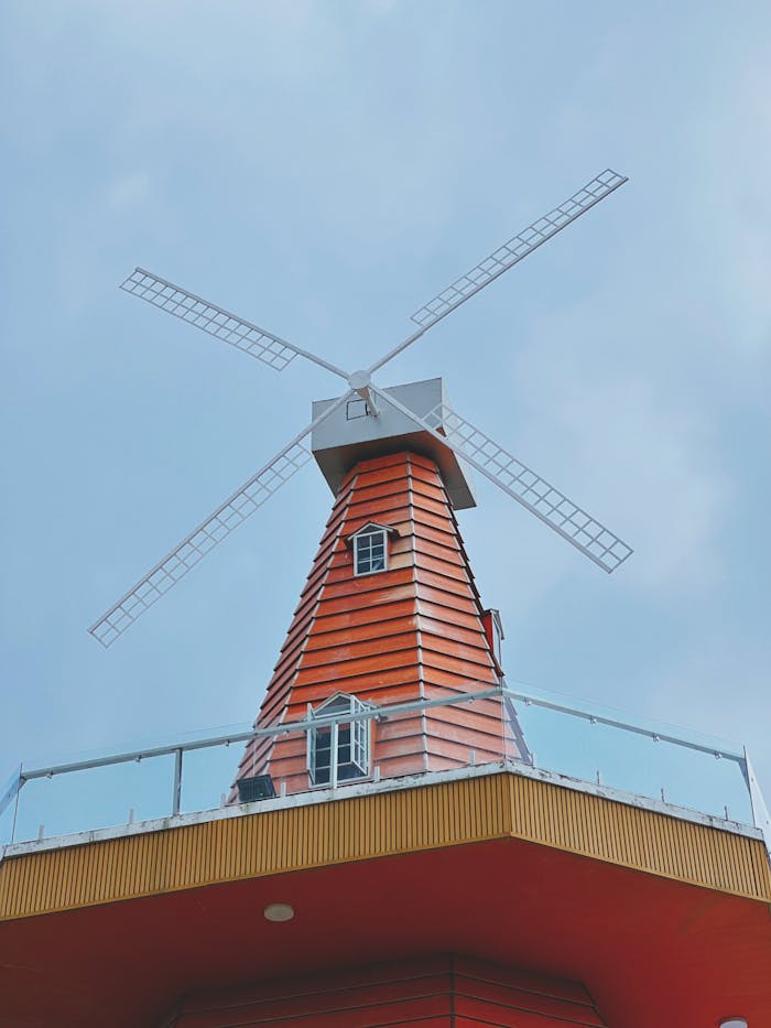 service-03 A red wooden windmill structure with white blades stands tall under a clear blue sky.